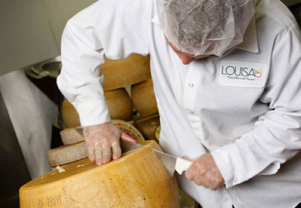 a Louisa chef cutting into a wheel of Parmesan cheese